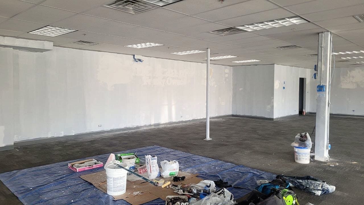 Before: Open commercial space with carpet tile and walls being patched