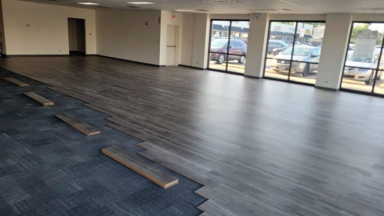 During: Plank flooring partly installed, with carpet tile still in place in the foreground